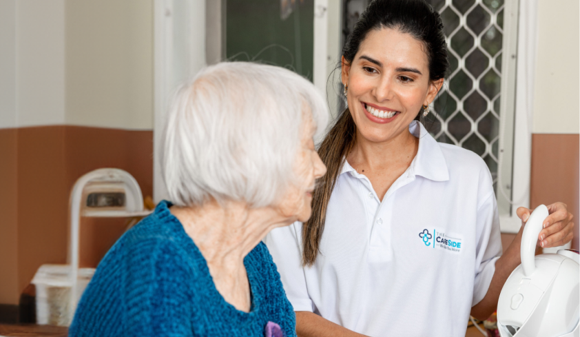 A caregiver from Carlisle Seniors Centre smiles while standing at the kitchen counter with her client and pouring cups of tea.