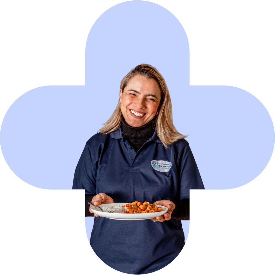 A photo of a caregiver from Carlisle Seniors Centre smiling and holding a plate of food.